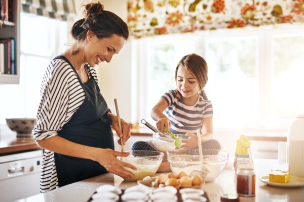 Schwangere Mutter und Kind backen gemeinsam in der Küche, Sicherheit und Hygiene beim Kochen, familiäre Küchenaktivität, fröhliche häusliche Atmosphäre beim Backen.