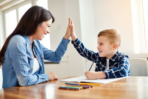 Mutter und Sohn geben sich ein High-Five über den Lernfortschritt, fröhliches Kind beim Lernen zu Hause, spielerische Erziehungsmethoden, familiäres Lernen mit Spaß.
