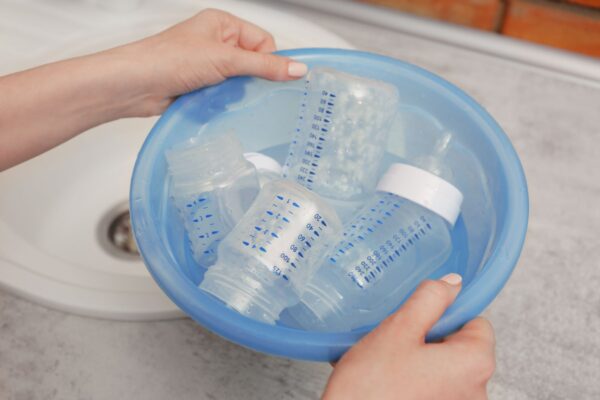 Hände einer Person, die Babyflaschen in einer Schüssel mit Wasser sterilisiert, um die Hygiene für die Babynahrung zu gewährleisten