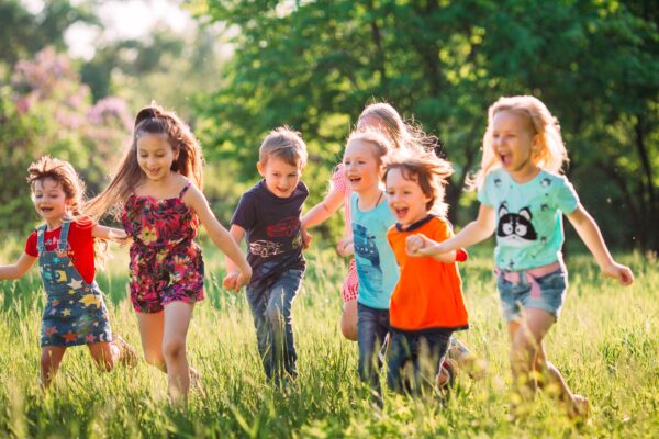 Fröhliche Kinder spielen und laufen auf einer grünen Wiese, um soziale Fähigkeiten und Freundschaft zu fördern
