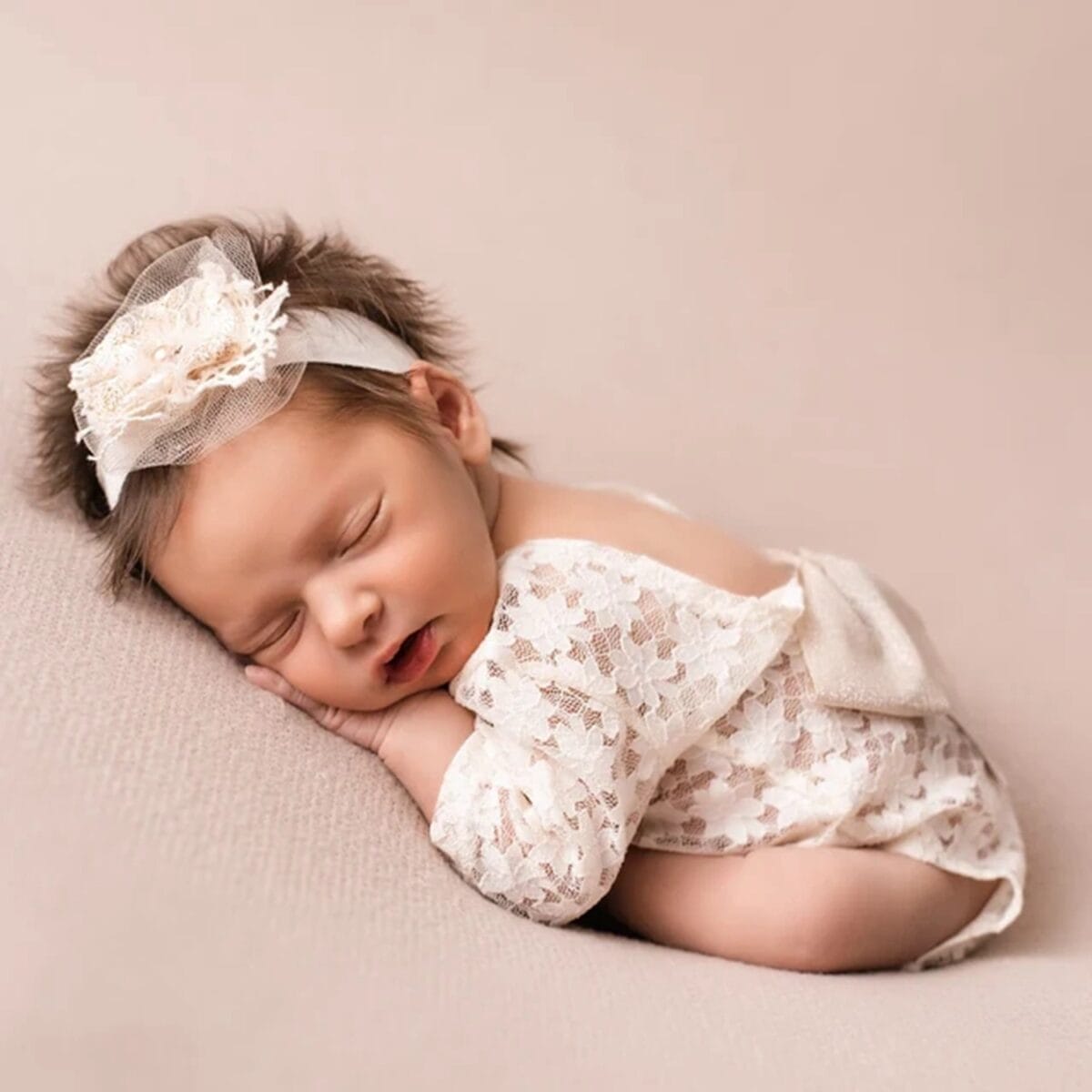Neugeborenes in einem zarten, rückenfreien Dreiecks-Strampler mit Spitze und passendem Haarband, ideal für Neugeborenenfotografie.