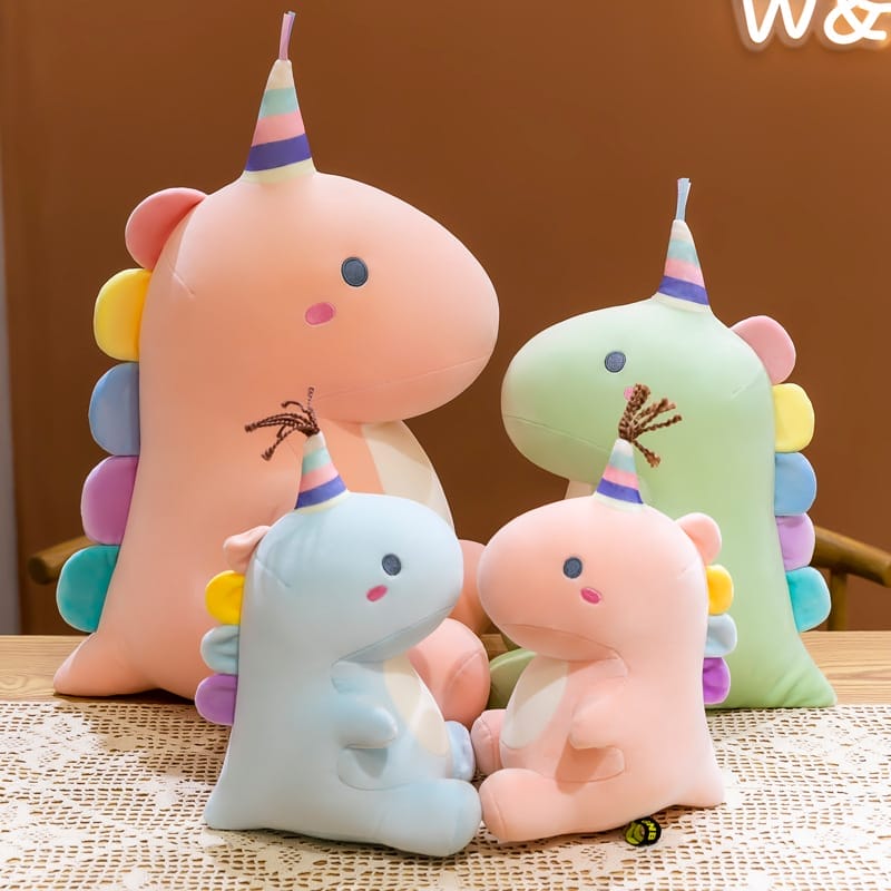 Eine Sammlung von vier freundlichen Dinosaurier-Plüschkissen in verschiedenen Pastellfarben, jeweils mit einem charmanten Partyhut. Diese kuscheligen Freunde sind perfekt zum Spielen, Schmusen und als hübsche Kinderzimmerdekoration.