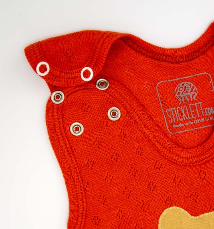 Nahaufnahme der verstellbaren Träger mit Druckknöpfen am rostroten Babystrampler aus Bio-Baumwolle.