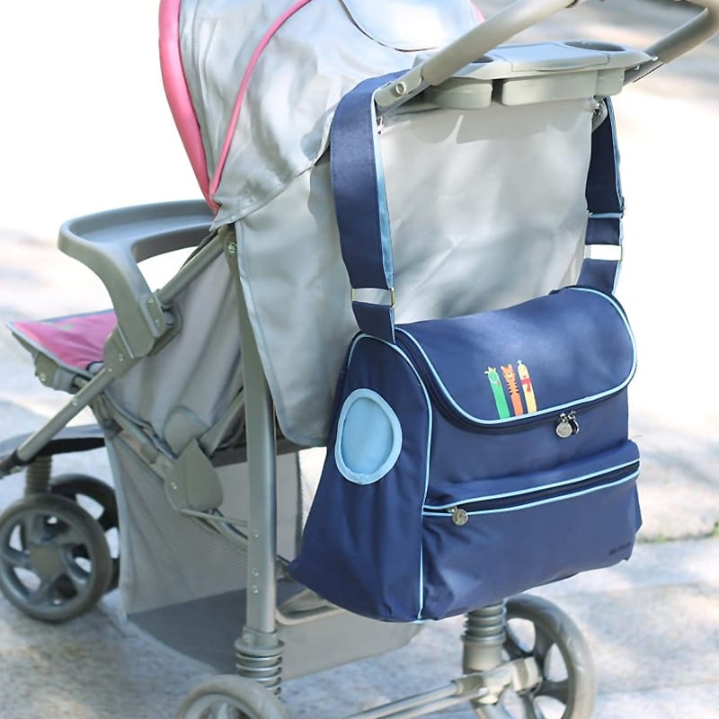 Frau trägt eine geräumige blaue Wickeltasche mit Kinderwagenbefestigung und praktischer Schulterriemen-Funktion in einem grünen Park.