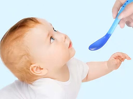 Baby schaut erwartungsvoll auf einen blauen Silikonlöffel beim Füttern.