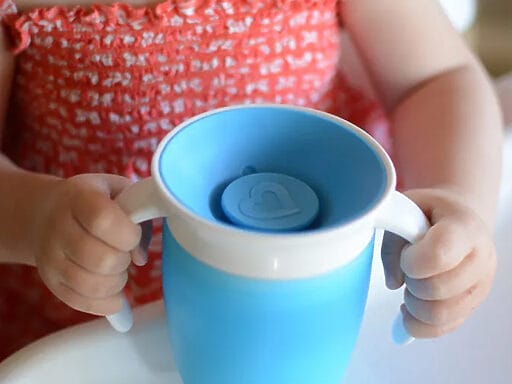 Kleinkind lernt selbstständig Trinken mit einem blauen Baby-Trinklernbecher, kinderfreundliches Design.